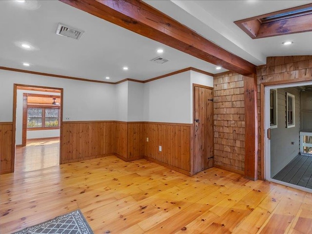 empty room featuring light wood-type flooring, visible vents, beam ceiling, and wainscoting