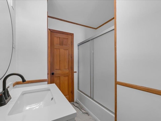 bathroom with a sink, marble finish floor, ornamental molding, and combined bath / shower with glass door