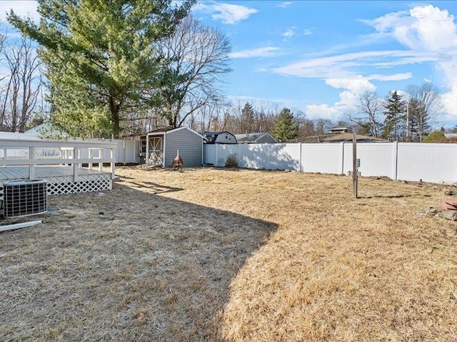 view of yard featuring central AC unit, a wooden deck, a fenced backyard, an outdoor structure, and a storage shed