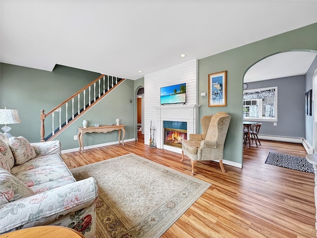 living room with arched walkways, light wood-type flooring, a fireplace, and stairs