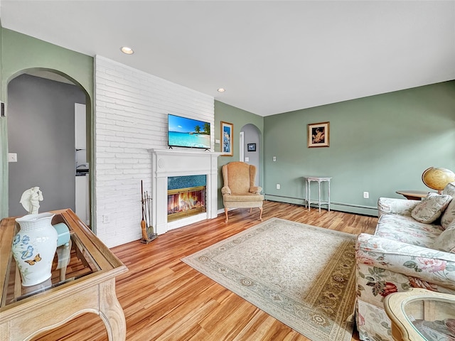 living room featuring arched walkways, a baseboard radiator, recessed lighting, wood finished floors, and a glass covered fireplace