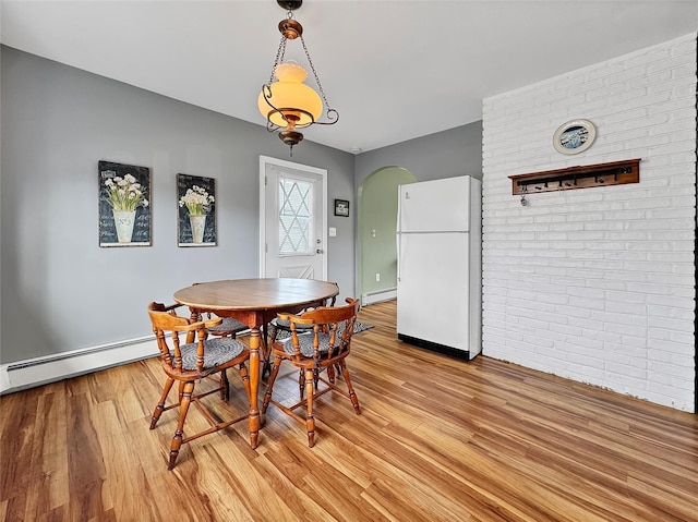 dining space featuring arched walkways, brick wall, light wood finished floors, and baseboard heating