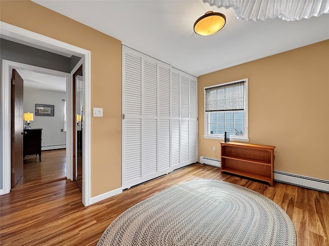 bedroom with a closet, baseboard heating, and wood finished floors