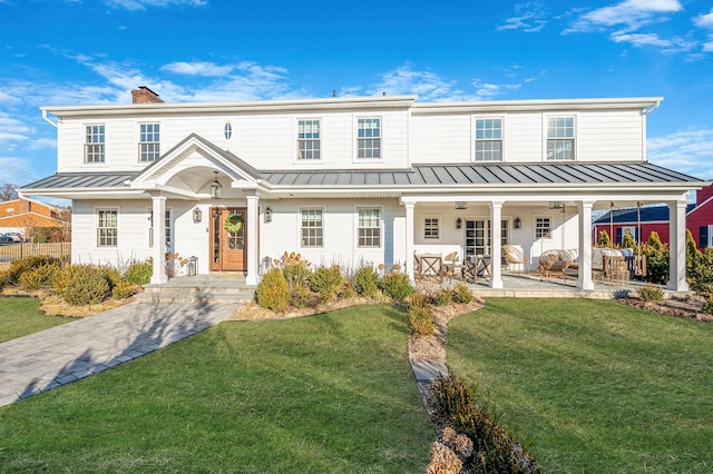 view of front of property featuring a chimney, a standing seam roof, fence, a patio area, and a front lawn