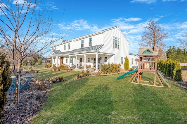 back of house featuring metal roof, a porch, a playground, a yard, and a standing seam roof