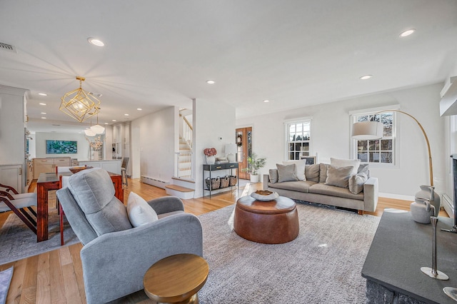 living room featuring a baseboard radiator, recessed lighting, visible vents, light wood-type flooring, and stairs