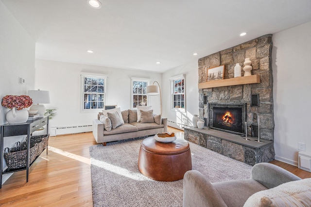 living area with a stone fireplace, a baseboard radiator, light wood-style flooring, and recessed lighting