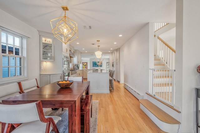 dining room featuring a baseboard radiator, visible vents, stairs, light wood-type flooring, and an inviting chandelier