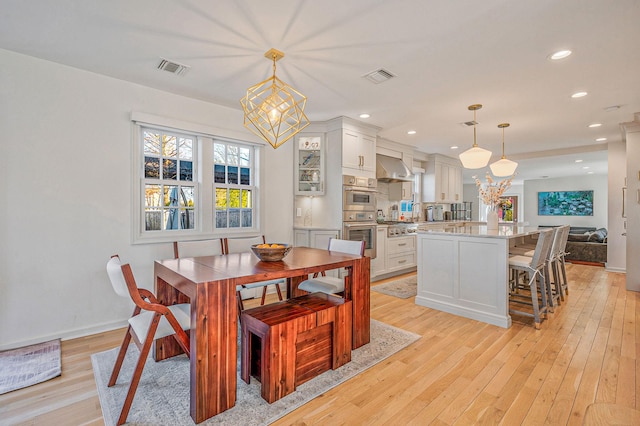 dining area with light wood-type flooring, visible vents, and a notable chandelier