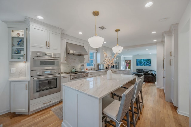 kitchen with visible vents, a kitchen island, open floor plan, stainless steel appliances, and wall chimney range hood