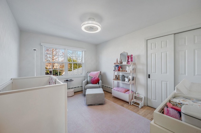 bedroom with a closet, a baseboard heating unit, and wood finished floors