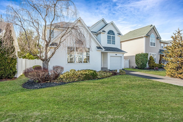 traditional-style house with driveway, an attached garage, fence, and a front yard