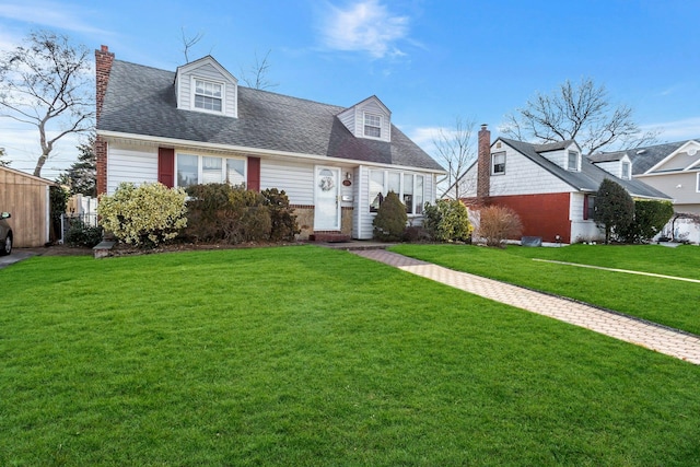 cape cod-style house featuring roof with shingles, a chimney, and a front yard