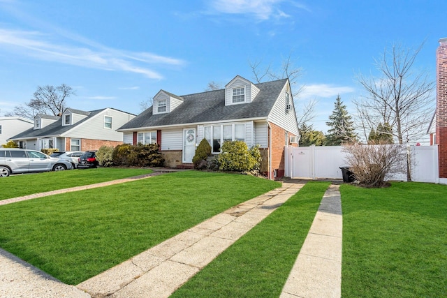 new england style home with a gate, a front yard, fence, and brick siding