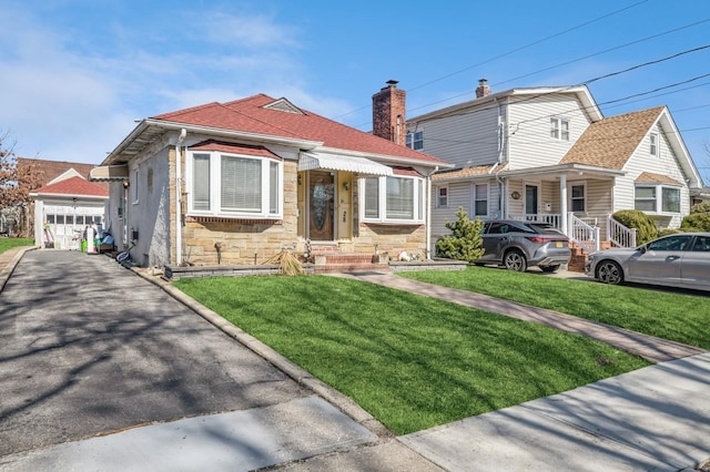 view of front of home with stone siding, a shingled roof, an outbuilding, and a front yard