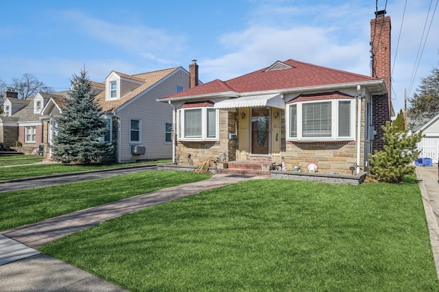 view of front of home with stone siding, roof with shingles, a chimney, and a front yard