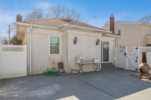 back of house with a patio, fence, roof with shingles, a gate, and stucco siding