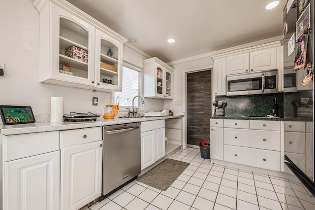 kitchen featuring tasteful backsplash, white cabinets, glass insert cabinets, appliances with stainless steel finishes, and a sink