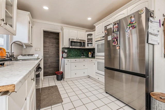 kitchen featuring light tile patterned floors, stainless steel appliances, a sink, white cabinets, and glass insert cabinets