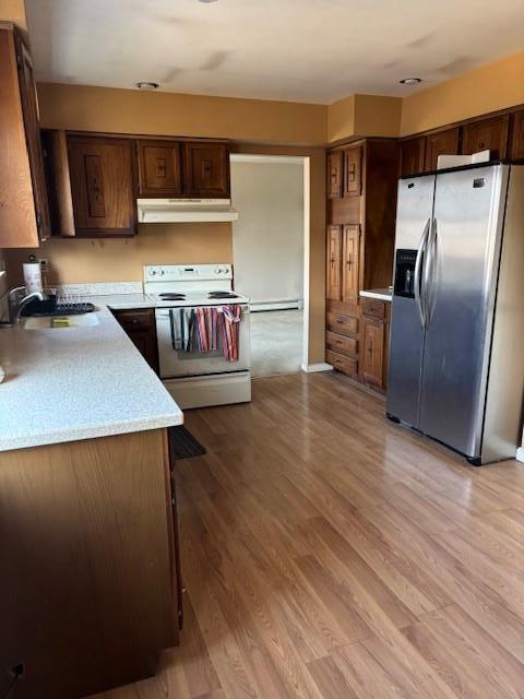 kitchen with stainless steel fridge, light countertops, light wood-type flooring, under cabinet range hood, and white range with electric cooktop