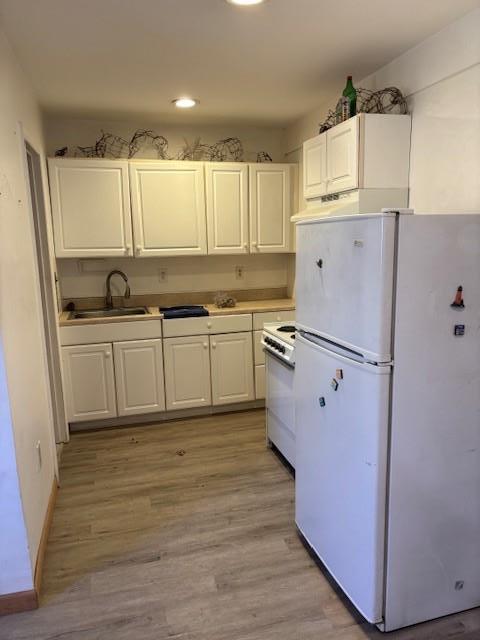 kitchen featuring light wood finished floors, white appliances, a sink, and white cabinets