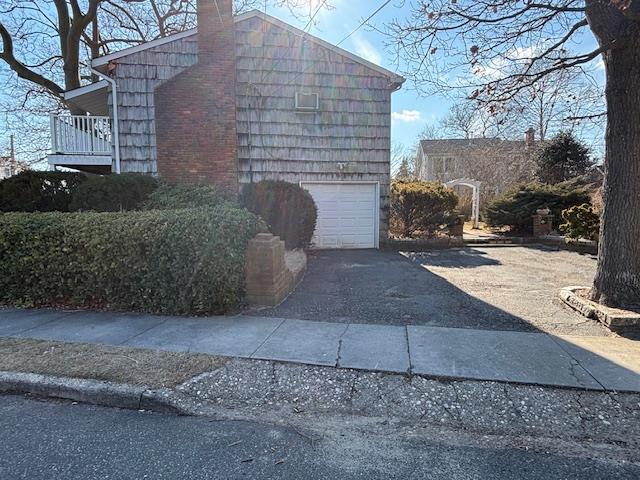 view of property exterior featuring driveway, a chimney, and an attached garage