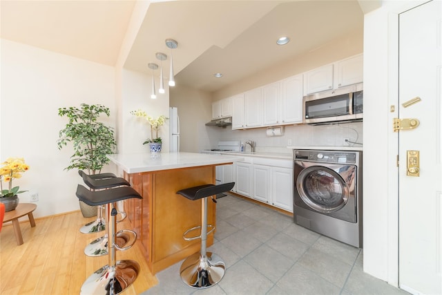 kitchen with white cabinets, light countertops, stainless steel microwave, a kitchen bar, and washer / dryer