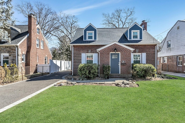 cape cod-style house with brick siding, roof with shingles, a front lawn, and fence