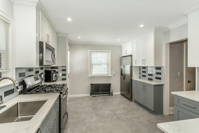 kitchen featuring light stone countertops, radiator heating unit, a sink, gray cabinetry, and stainless steel appliances