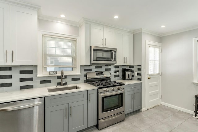 kitchen with gray cabinetry, ornamental molding, decorative backsplash, appliances with stainless steel finishes, and a sink