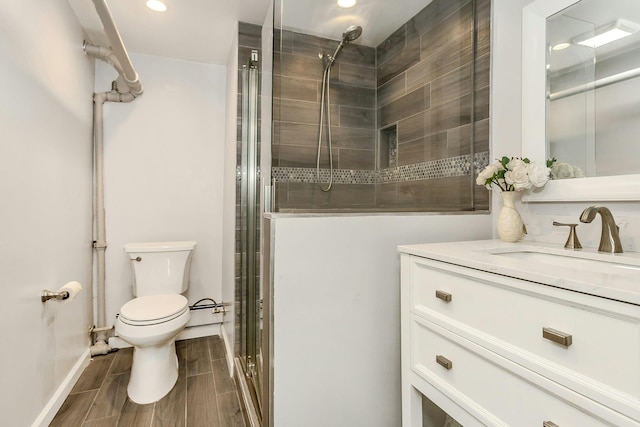 bathroom with wood finish floors, toilet, recessed lighting, tiled shower, and vanity