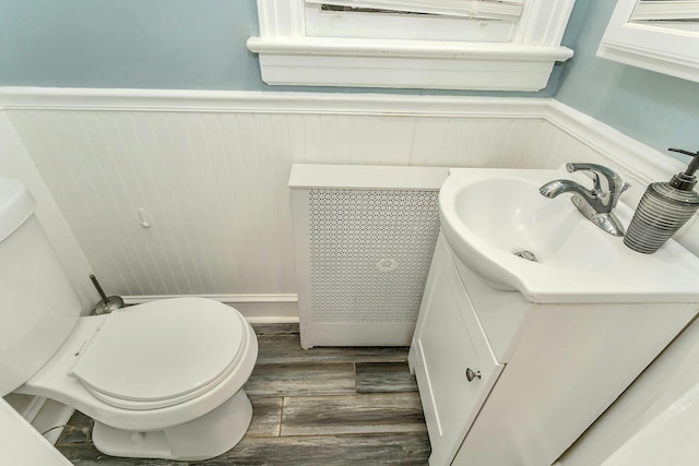 bathroom with vanity, toilet, wood finished floors, and wainscoting