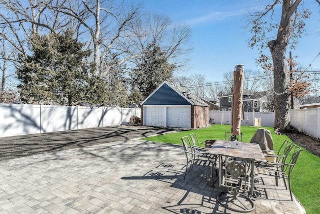 view of patio / terrace with a detached garage, an outbuilding, a fenced backyard, and outdoor dining space