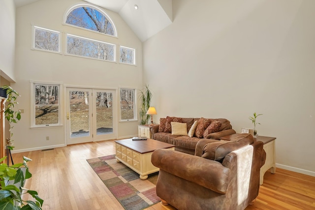 living room with high vaulted ceiling, light wood-type flooring, and baseboards