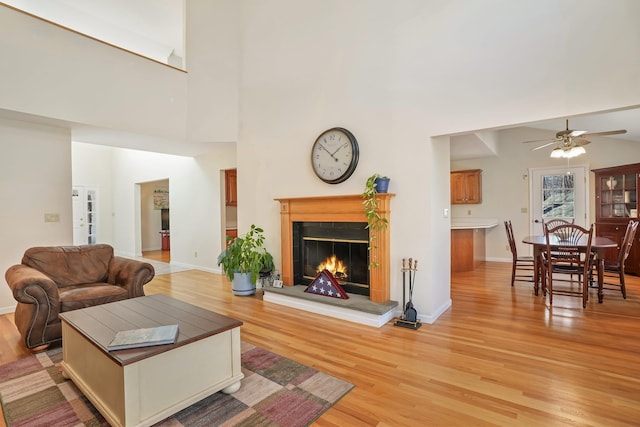 living room featuring light wood-style flooring, a lit fireplace, baseboards, and a ceiling fan