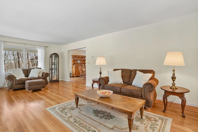 living area featuring light wood-style floors, baseboards, and arched walkways