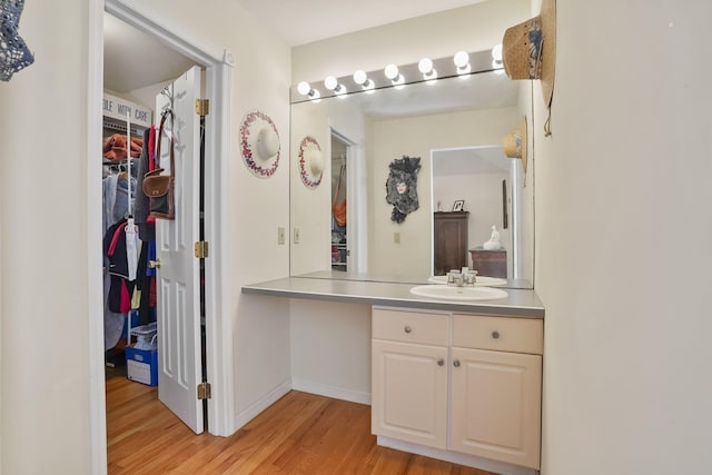 bathroom featuring a walk in closet, vanity, baseboards, and wood finished floors