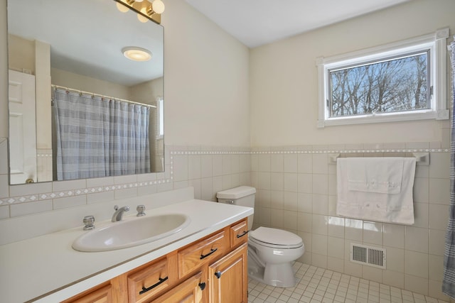 bathroom with tile patterned flooring, toilet, vanity, visible vents, and tile walls