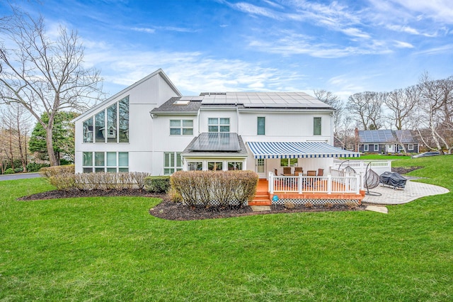 rear view of house featuring a patio area, a deck, solar panels, and a lawn