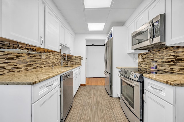 kitchen featuring a paneled ceiling, backsplash, appliances with stainless steel finishes, white cabinets, and a sink