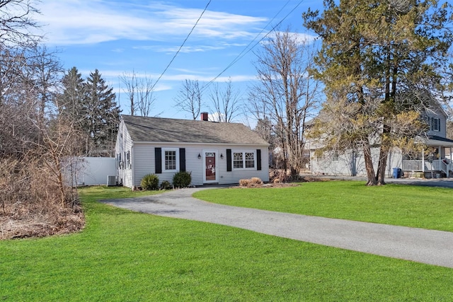 view of front facade with a shingled roof, a front lawn, fence, cooling unit, and driveway