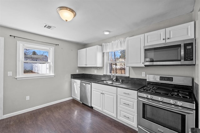 kitchen featuring visible vents, dark wood finished floors, a sink, stainless steel appliances, and dark countertops