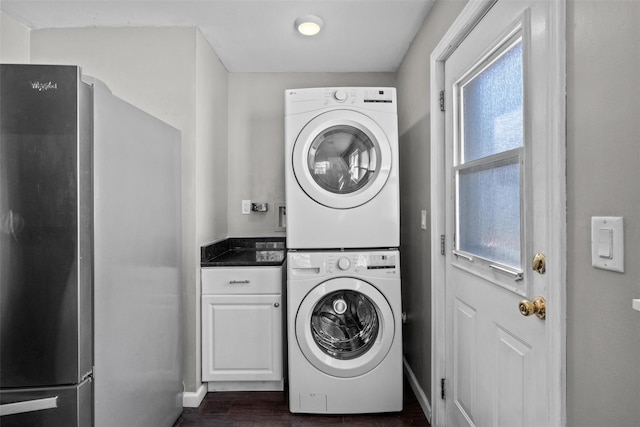 laundry area with dark wood-style floors, cabinet space, stacked washer and clothes dryer, and baseboards