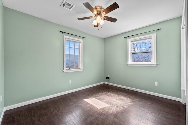 spare room with a wealth of natural light, visible vents, baseboards, and dark wood-style floors