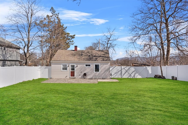 back of house featuring roof with shingles, a fenced backyard, a chimney, a patio area, and a lawn