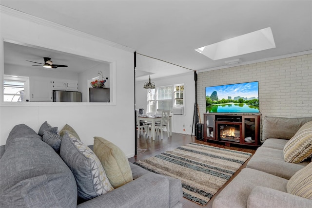 living area featuring brick wall, ornamental molding, wood finished floors, and a glass covered fireplace