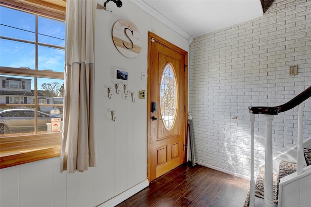 foyer entrance featuring dark wood-type flooring, crown molding, brick wall, and stairs