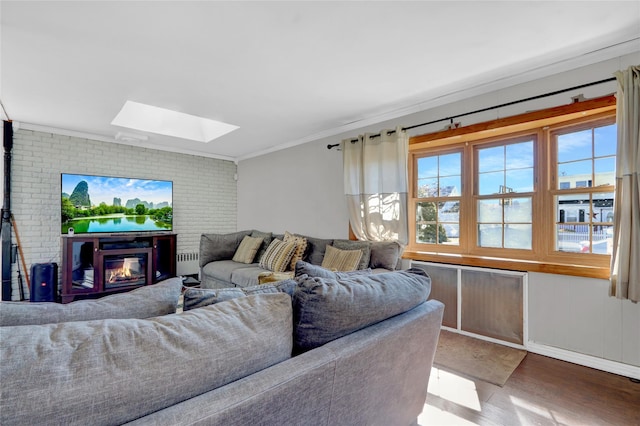 living area featuring a skylight, ornamental molding, a glass covered fireplace, brick wall, and wood finished floors