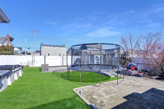 view of yard featuring a trampoline, a fenced backyard, and a patio