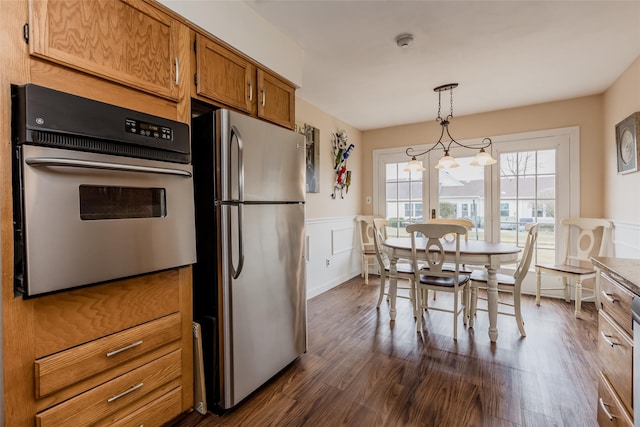 kitchen featuring a wainscoted wall, brown cabinets, stainless steel appliances, a decorative wall, and dark wood-type flooring